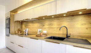 A modern kitchen with a wooden backsplash, a black sink, and a built-in oven. - Casa Allegrini - VICO (VICO)