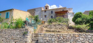 A stone staircase leading to a stone building with a tower, surrounded by greenery and a stone wall. - Coté village-Nelly - CRISTINACCE (CRISTINACCE)