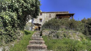 Ein Steinhaus mit einer Treppe, die zu einer Tür führt, umgeben von viel Grün.