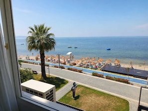 Vista de una playa con sombrillas, una palmera y un camino que lleva a la playa.