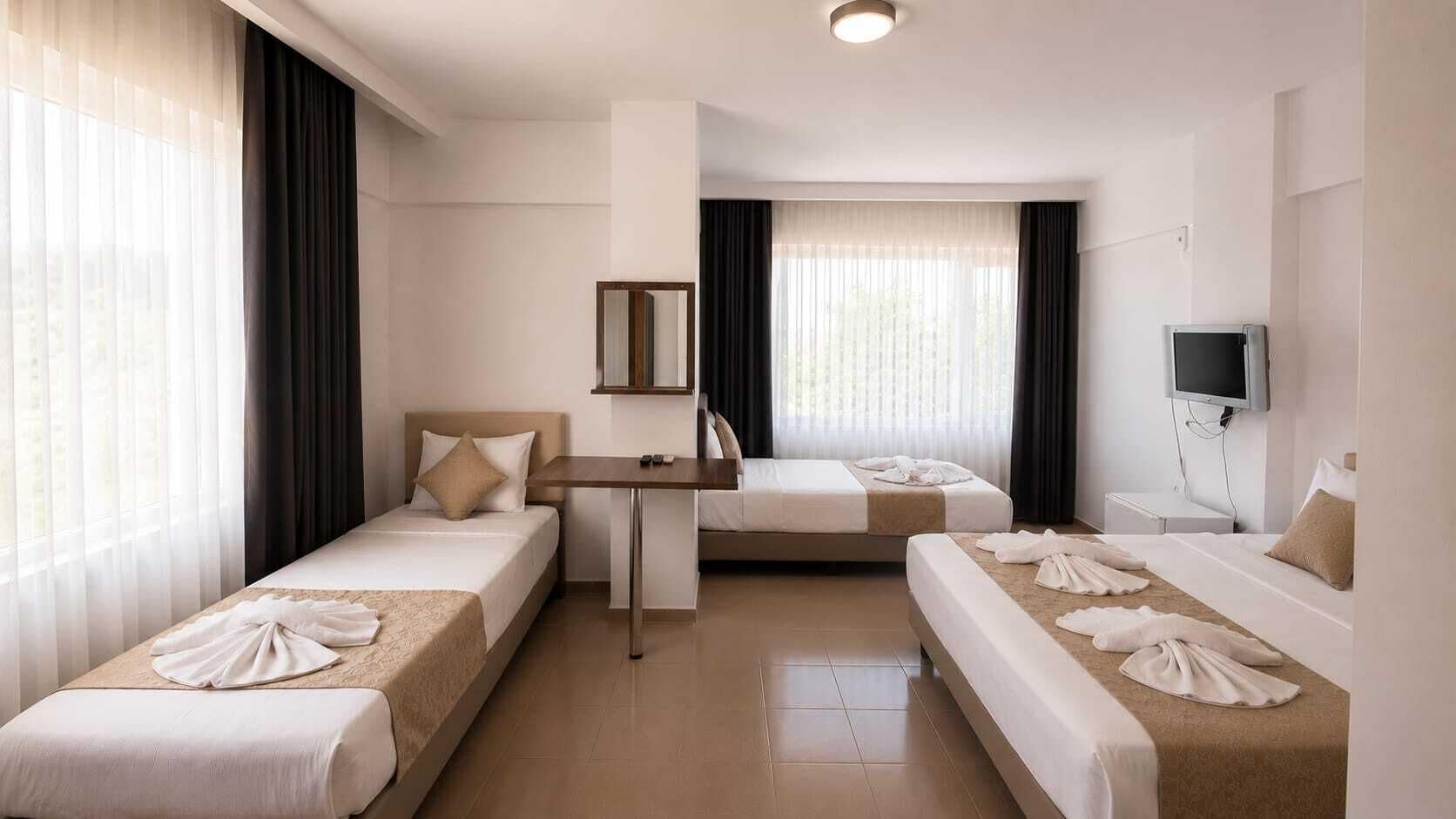 Habitación de hotel con tres camas, un escritorio, un televisor y una ventana con cortinas.