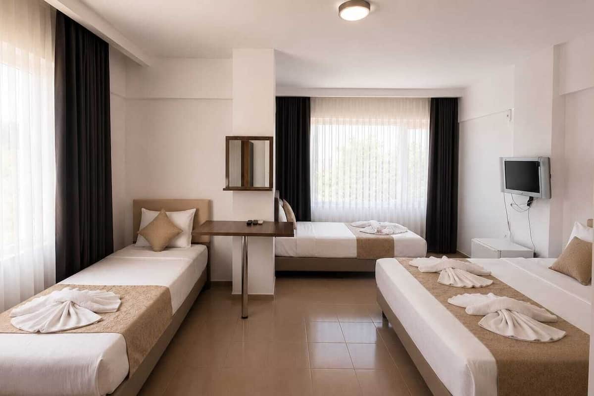 A hotel room with three beds, a desk, a TV, and a window with curtains.