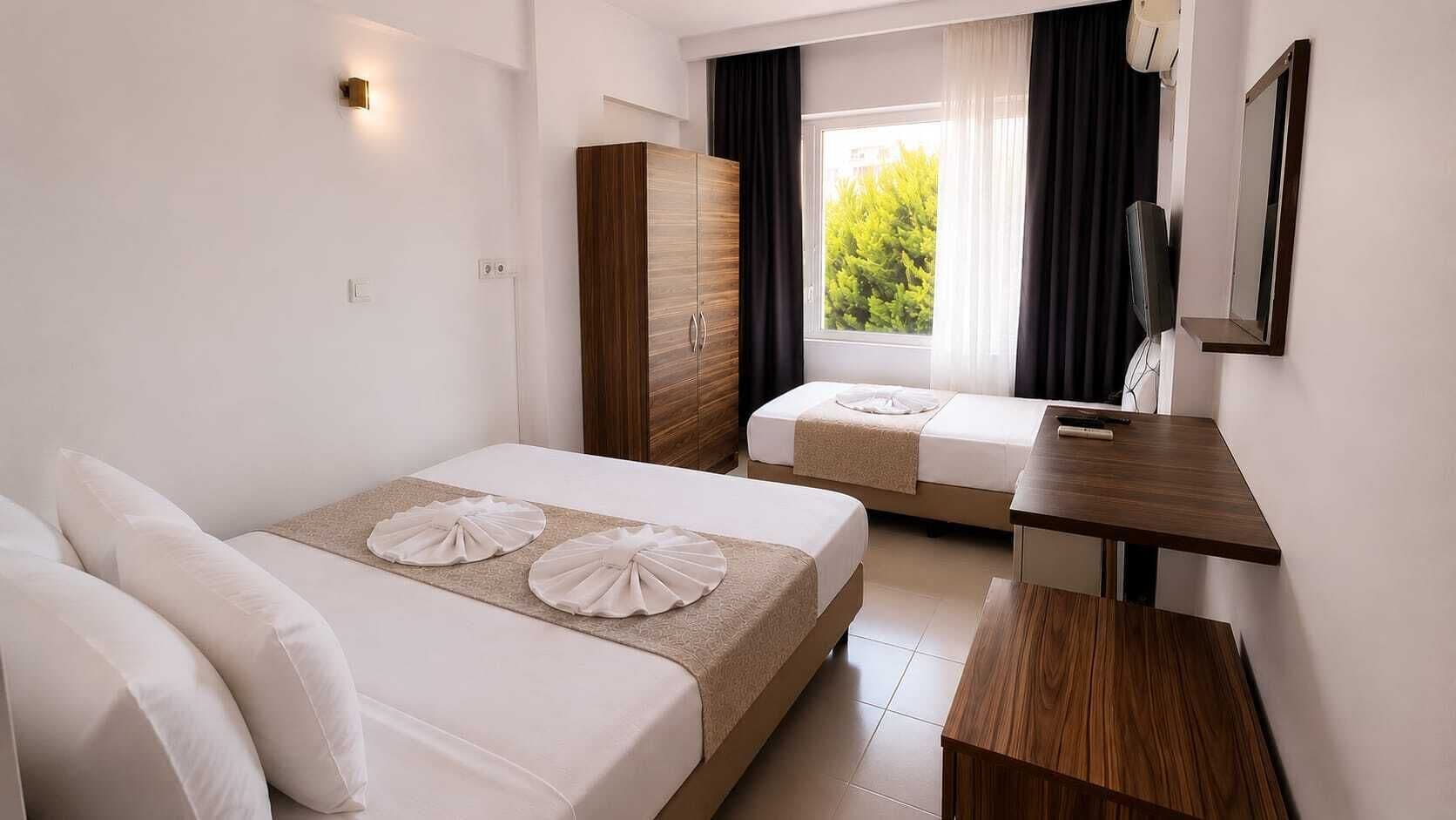 Habitación de hotel con dos camas, un armario de madera, un escritorio pequeño y una ventana con cortinas.