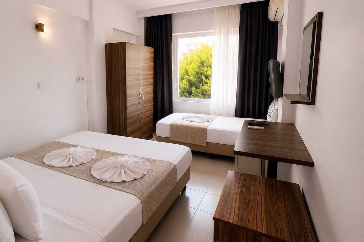 A hotel room with two beds, a wooden wardrobe, a small desk, and a window with curtains.