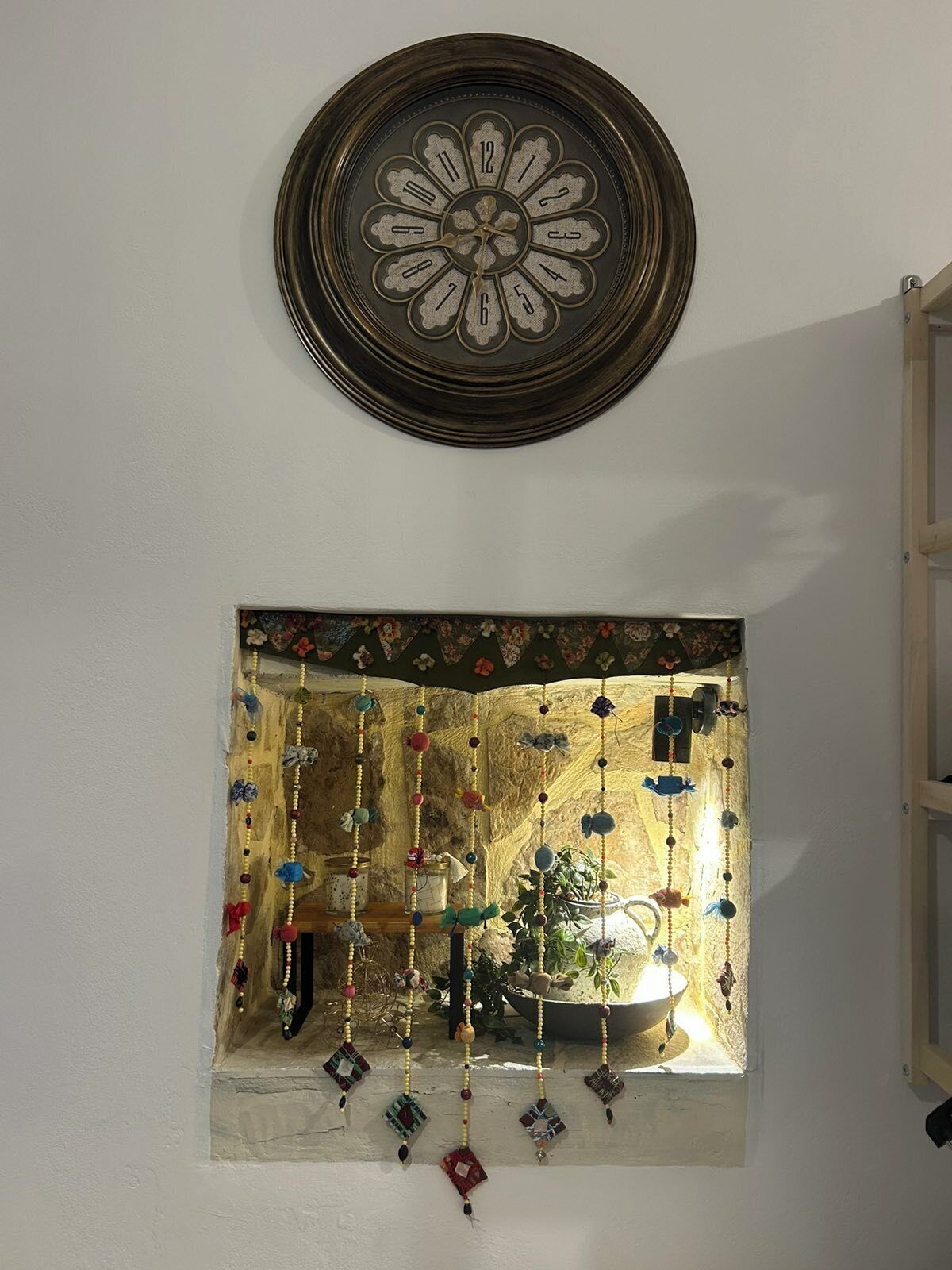 Eine Wanduhr mit floralem Dekor, ein Spiegel mit Zierrahmen und ein hängendes Ornament mit Perlen und geometrischen Formen.