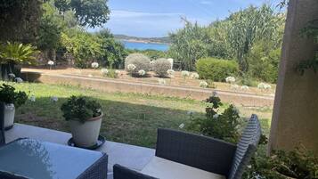 Une terrasse dotée de meubles en osier, de plantes en pot et offrant une vue sur un paysage côtier.