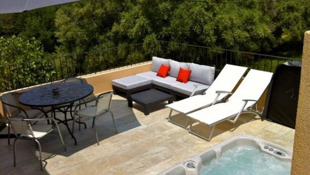 Eine Dachterrasse mit Whirlpool, Liegestühlen, einer Couch mit roten Kissen und einem Tisch mit Stühlen.
