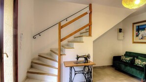 Una escalera con barandillas de madera, una máquina de coser sobre una mesa y un sofá verde en una habitación con paredes blancas.