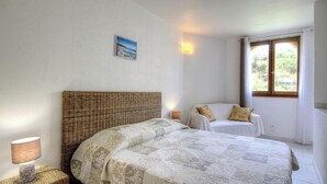 Un dormitorio con cama, mesita de noche, lámpara, silla, ventana y luz empotrada en la pared.