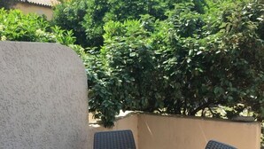 Un patio con una mesa y cuatro sillas, rodeado de follaje y una pared.