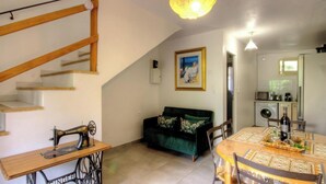 Una sala de estar con una escalera, una máquina de coser, un sofá verde, una mesa de comedor con sillas y una cocina al fondo.