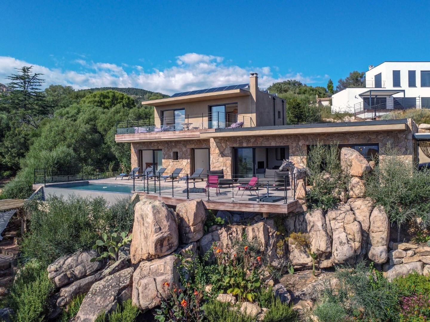 A modern house with a pool, stone facade, and a view of the surrounding landscape.