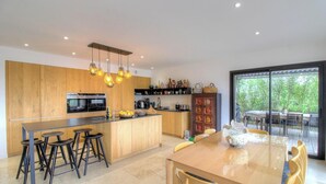 A modern kitchen with wooden cabinets, a central island, bar stools, and pendant lighting. - Villa Rocher - SAINTE LUCIE DE PORTO VECCHIO (SAINTE LUCIE DE PORTO VECCHIO)