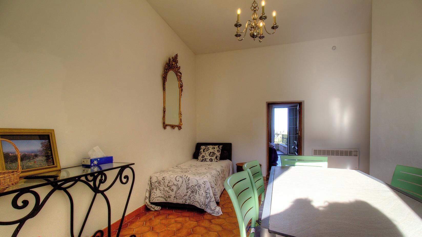 Ein Schlafzimmer mit Bett, Tisch, Stuhl, Spiegel und einer Deckenleuchte.
