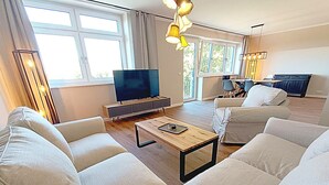 Ein modernes Wohnzimmer mit einer Sofagarnitur, einem Couchtisch, einem Fernseher und einem Essbereich mit Stühlen.