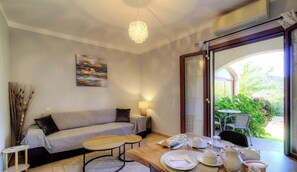 A modern living room with a sofa, coffee table, and dining area with a table set for two. - Residence U Filipaghju 1 (GALERIA)