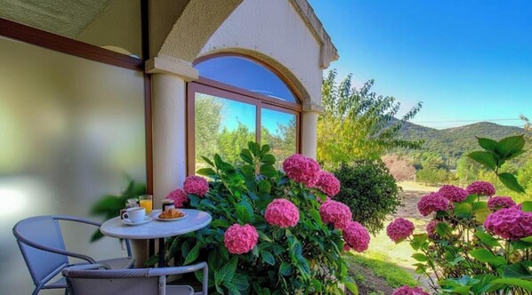 A patio with a table, chairs, and a view of a garden with pink flowers and greenery. - Residence U Filipaghju 1 (GALERIA)