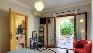 A room with a washing machine, a TV, a glass door leading to an outdoor area with plants, and a red chair. - Residence U Filipaghju 1 (GALERIA)