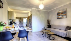 A modern living room with a sofa, two round tables, and a dining area with chairs and a table set for breakfast. - Residence U Filipaghju 1 (GALERIA)
