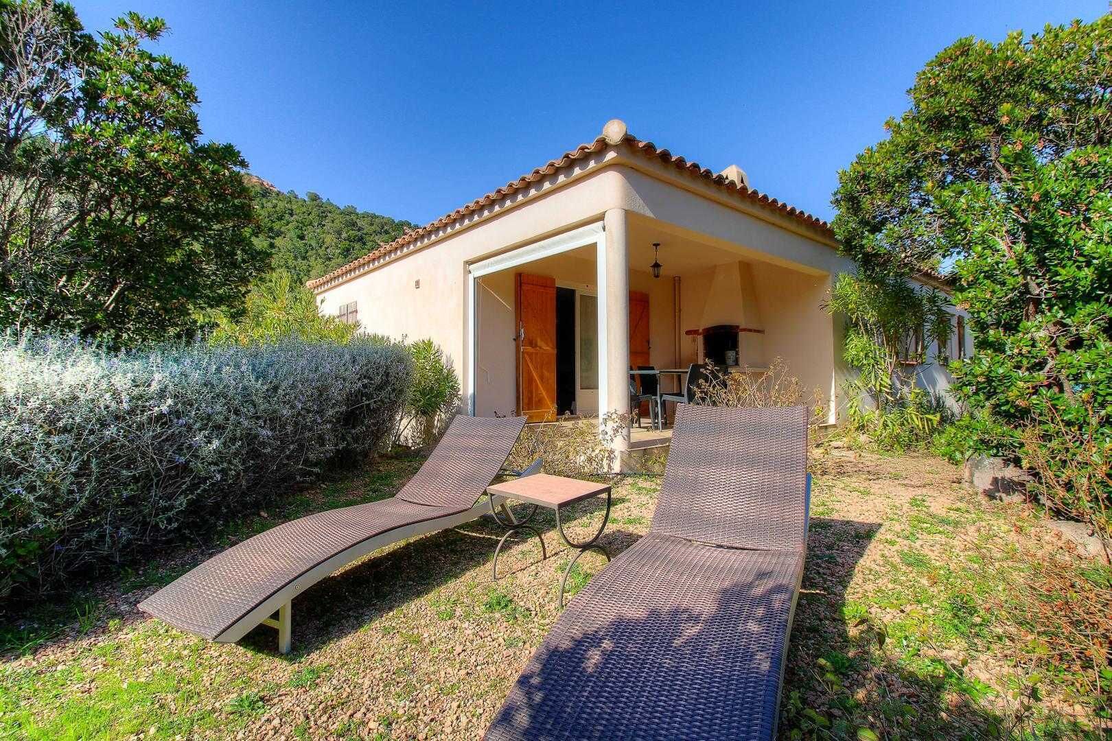 A villa with a covered patio, two lounge chairs, and a small table.