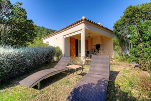 Eine Villa mit überdachter Terrasse, zwei Liegestühlen und einem kleinen Tisch.