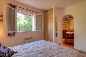 Ein Schlafzimmer mit Bett, Fenster, Heizkörper und Blick ins Badezimmer.