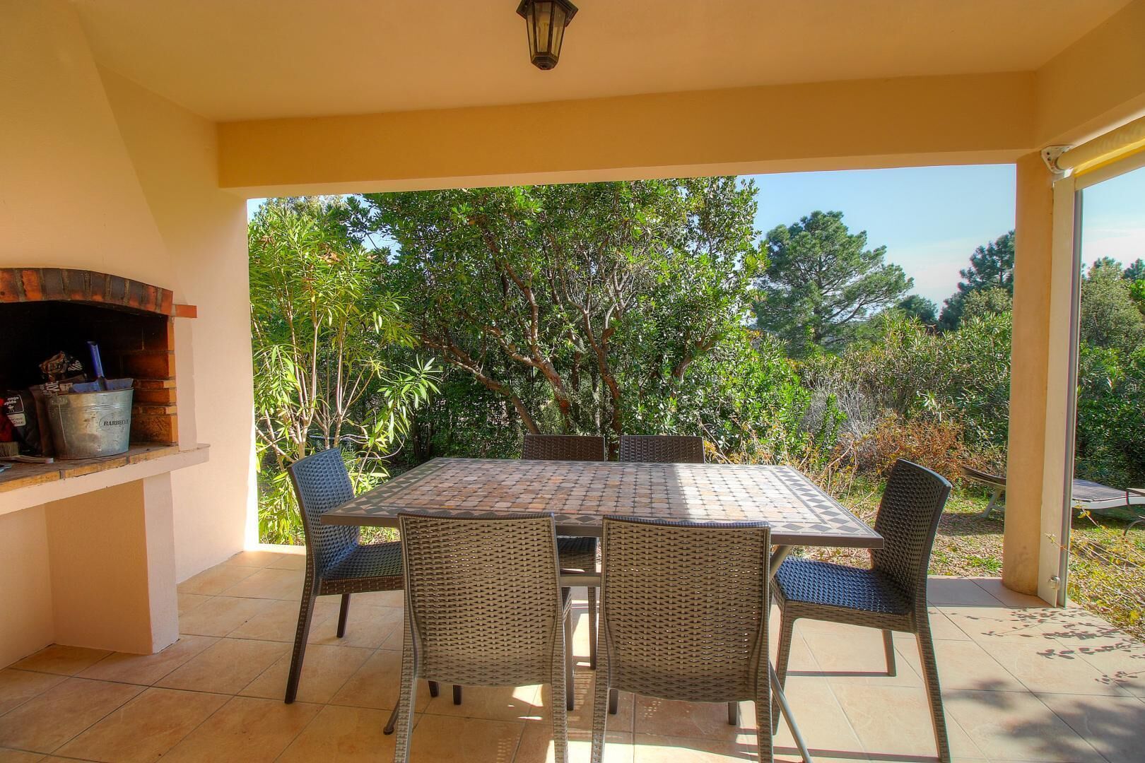 An outdoor patio with a table and chairs, a grill, and a view of trees.