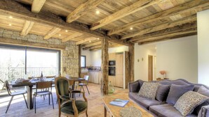 A rustic interior with a stone wall, wooden beams, a dining area, a sofa, and a kitchen. - Casa Scaledda - BOCOGNANO (BOCOGNANO)