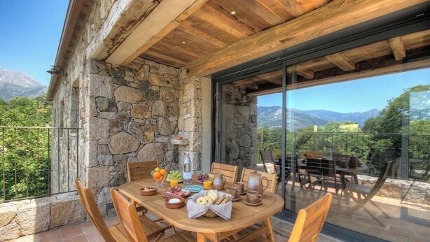 A dining area with a stone wall, wooden ceiling, and a table set for breakfast with various food items and drinks. - Casa Scaledda - BOCOGNANO (BOCOGNANO)
