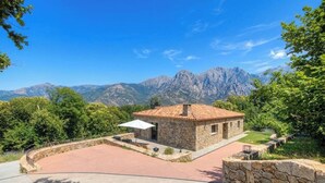 A stone building with a red-tiled roof, surrounded by a paved area, and set against a backdrop of mountains. - Casa Scaledda - BOCOGNANO (BOCOGNANO)