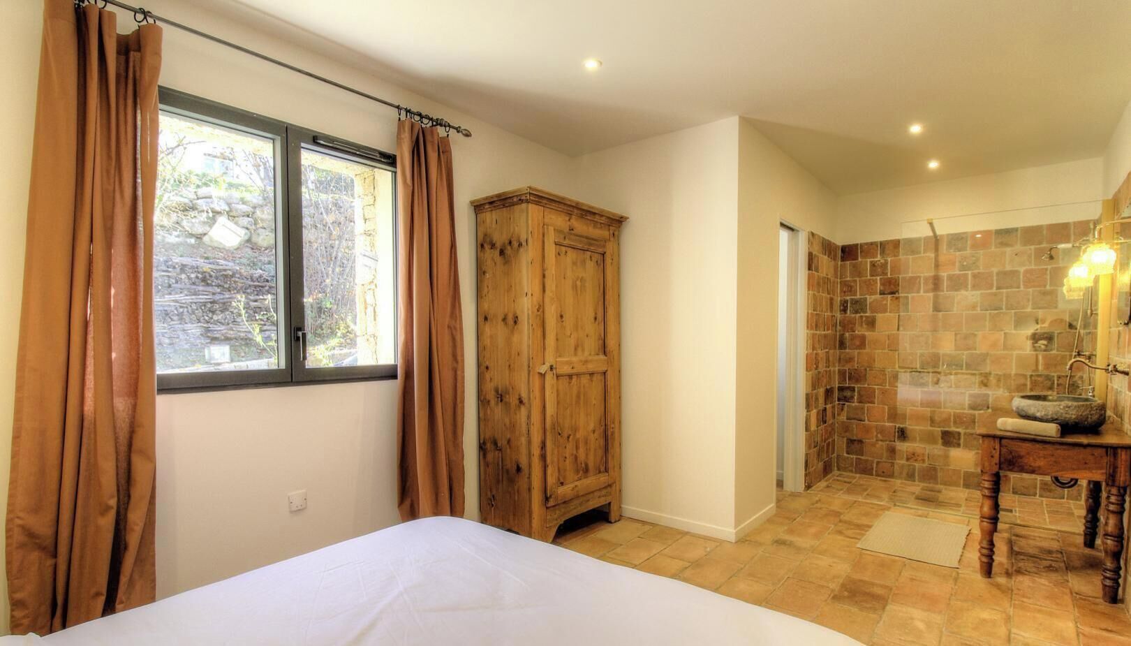 Une chambre à coucher avec un lit, une armoire en bois et une salle de bain avec un mur en pierre et un lavabo.
