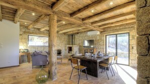 A rustic interior with exposed wooden beams, stone walls, a stone fireplace, a dining area with chairs, and a large window. - Casa Scaledda - BOCOGNANO (BOCOGNANO)