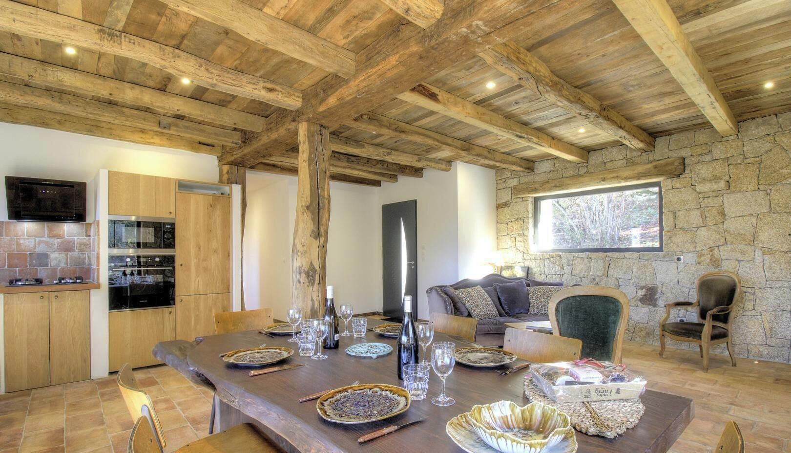 Un coin repas rustique avec une table en bois dressée pour le repas, des murs en pierre et une cheminée en pierre.