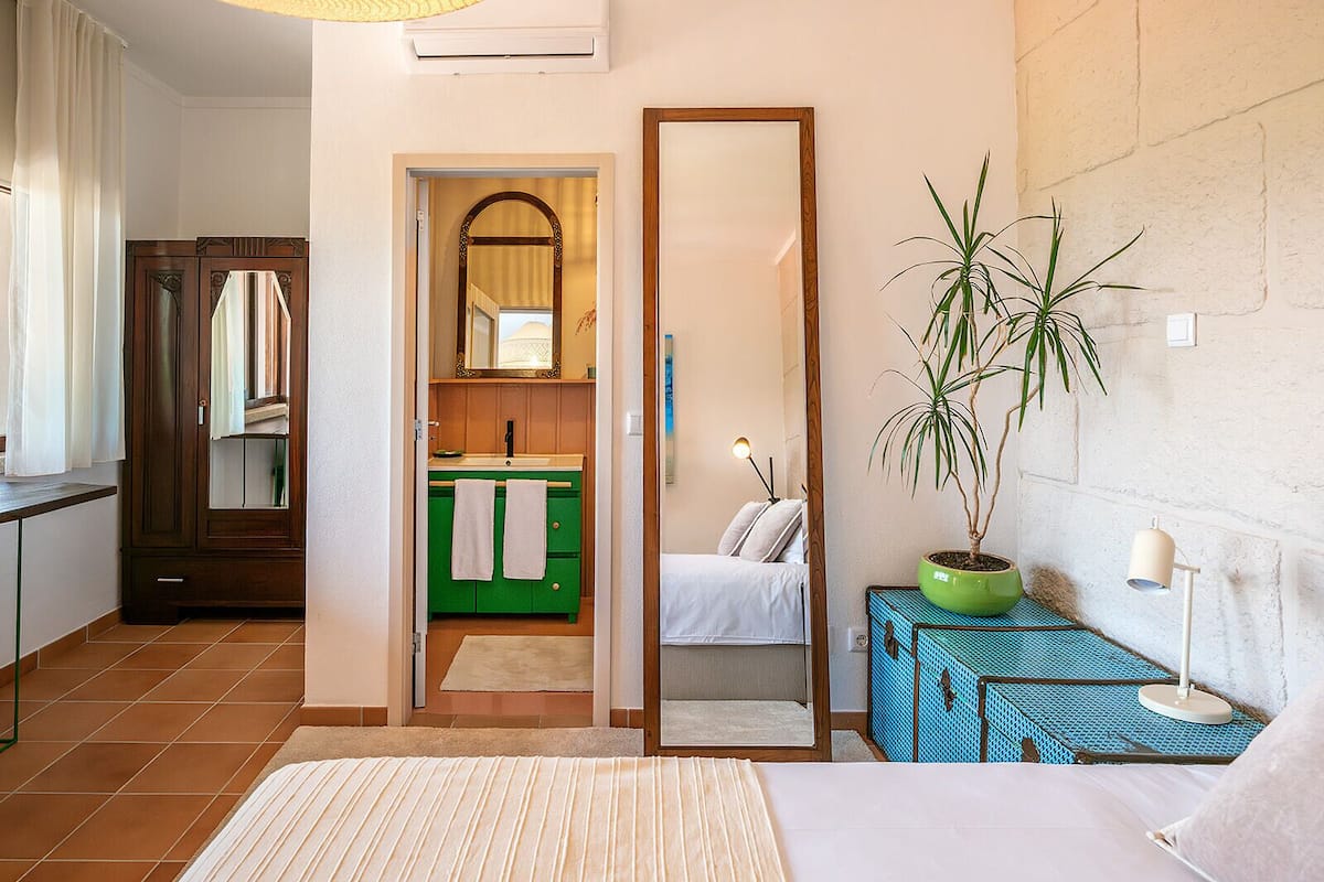 A bedroom with a bed, a mirror, a green cabinet, a potted plant, and a bedside table.