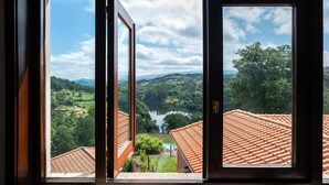 Uitzicht door een raam met houten kader, waarop een landschap met terrassen en een wateroppervlak zichtbaar is.