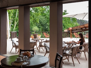An outdoor patio with wicker furniture, a round table with a vase, and a view of greenery. - TAMACA nature (Marco de Canaveses)