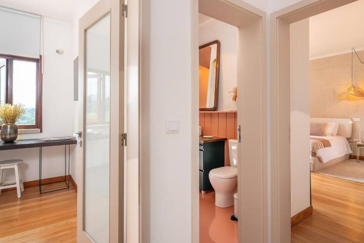 A modern interior with a wooden floor, a desk with a chair, a bathroom with a toilet and sink, and a bedroom with a bed and bedside table.