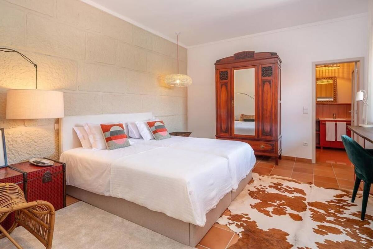 A bedroom with a bed, a wooden wardrobe, a desk, and a chair.