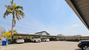 A parking lot with several cars, a palm tree, and a building with a flat roof. - H-Hub BBT (Bang Bua Thong)