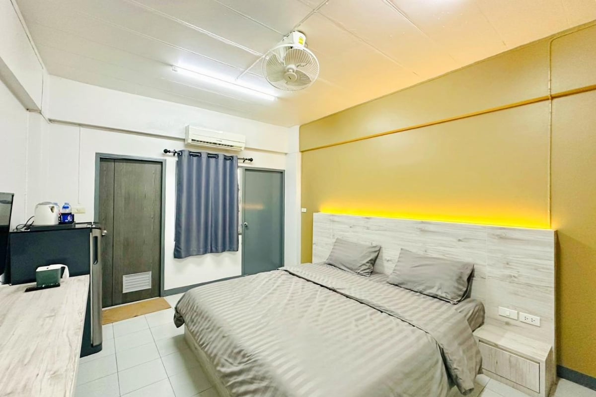 A bedroom with a bed, bedside table, nightstand, desk, and an air conditioning unit.