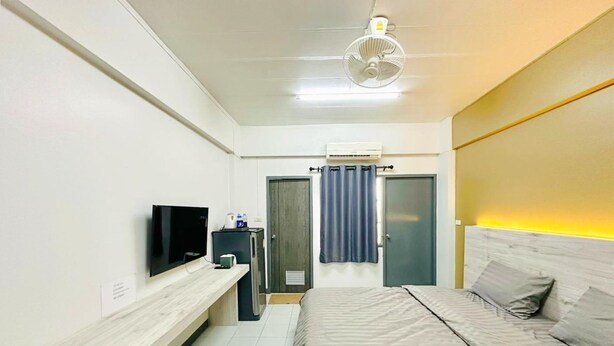 A bedroom with a bed, a TV, a desk, a fan, and a door. - H-Hub BBT (Bang Bua Thong)