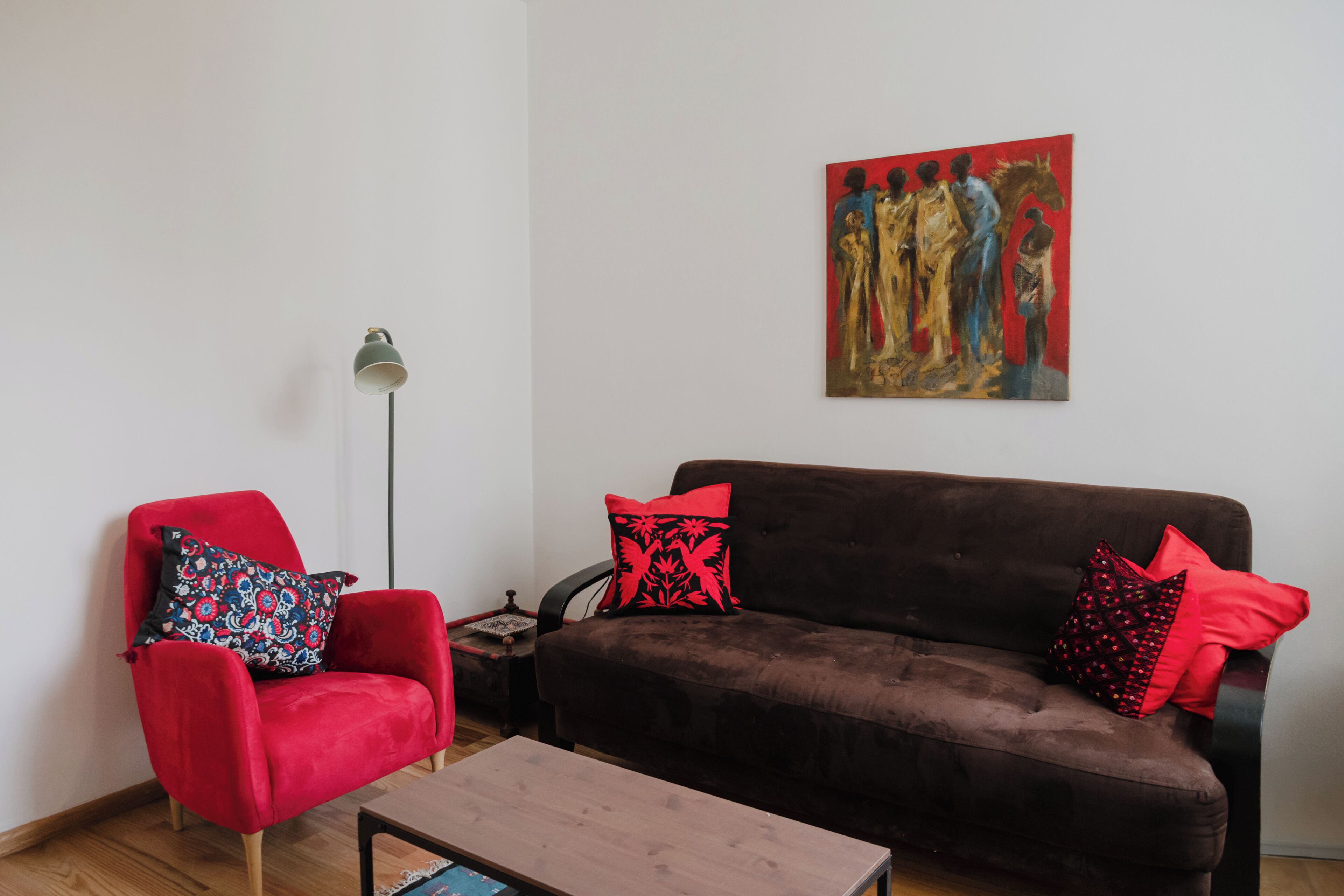 A living room with a red armchair, a brown sofa, and a painting on the wall.