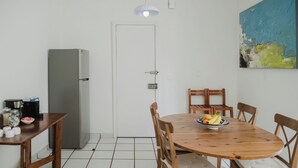 A dining area with a wooden table, chairs, a bowl of fruit, a refrigerator, and a door. - Beautiful 1BR in the heart of Condesa featuring a spacious equipped kitchen, cozy TV lounge, full bathroom, washer, and comfortable bedroom. Sofa bed available for 1 child. Perfect for enjoying one of CDMX’s best neighborhoods. (Cuauhtémoc)