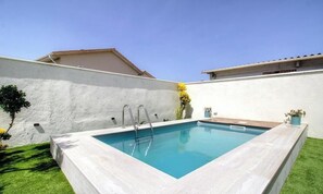 Ein rechteckiger Swimmingpool mit einer Metallleiter, umgeben von einer weißen Mauer und einer Rasenfläche.