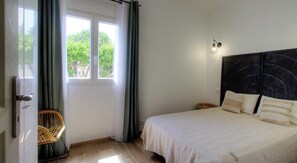 Ein Schlafzimmer mit Bett, Stuhl, Fenster und einer Wandleuchte.
