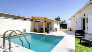 Ein Pool mit einer Holz-Pergola, einer Terrasse und einem Gebäude mit weißer Fassade.