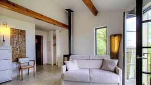 Una sala de estar con sofá, una silla de madera, pared de piedra, chimenea y ventana.