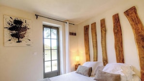 Un dormitorio con cama, ventana, puerta y vigas de madera en la pared.