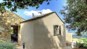 Un edificio de piedra con fachada color beige, una ventana pequeña con contraventanas y una puerta que da a un interior con un sofá.