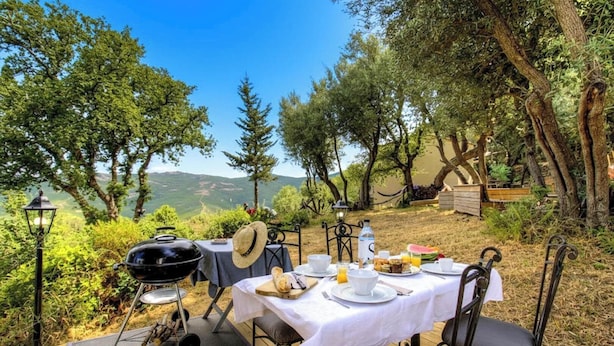 Un espacio exterior para comer con mesa, sillas, una parrilla y vistas a un paisaje montañoso.
